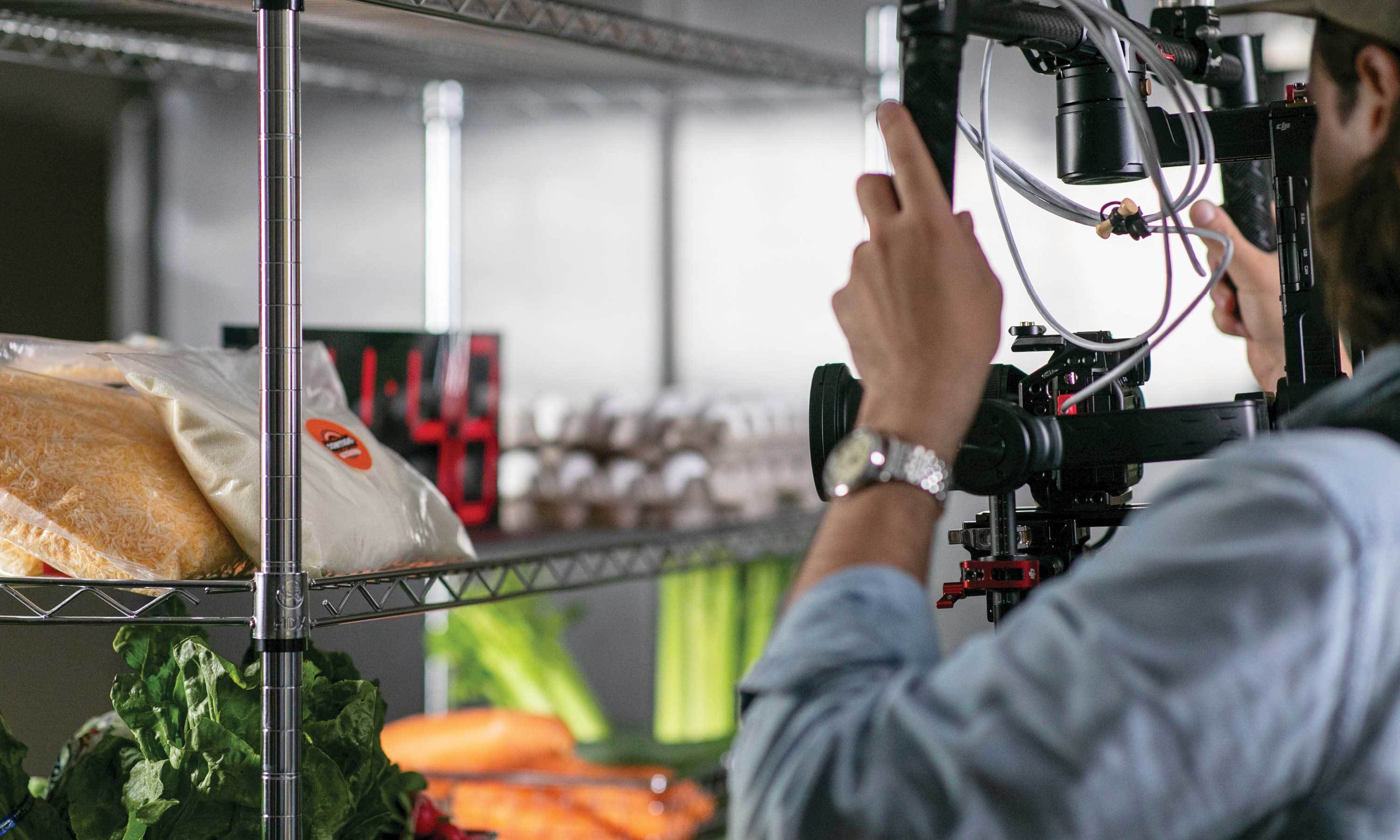 A man holding a camera while filming a close up shot of a restaurant kitchen shelf.